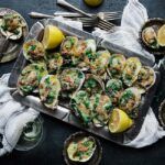 oysters covered in spinach and cheese on a serving tray with lemon
