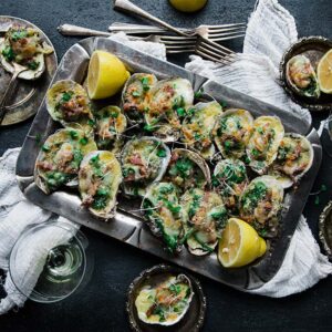 oysters covered in spinach and cheese on a serving tray with lemon
