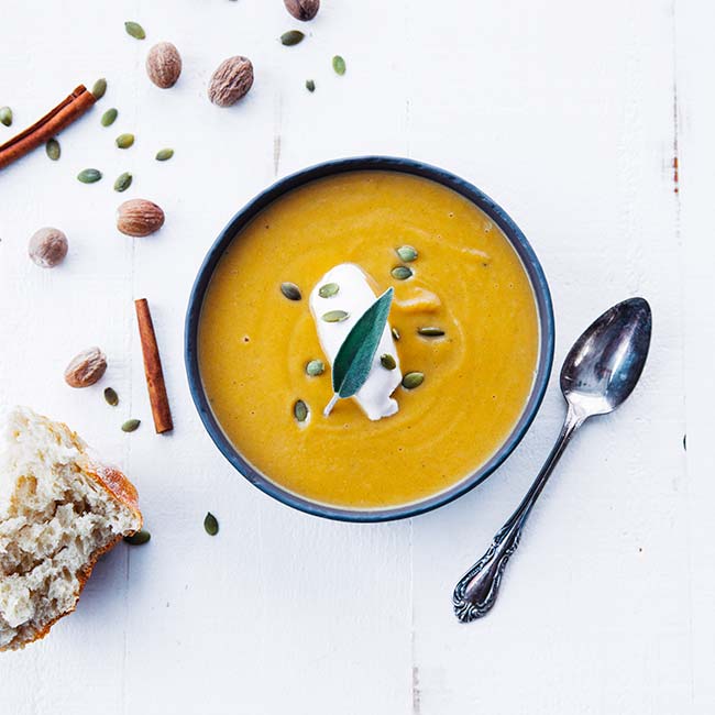 butternut squash soup in a bowl with cream, pumpkin seeds and sage