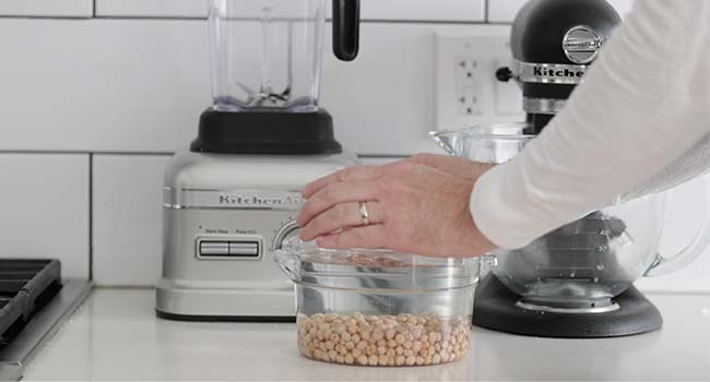 dried chickpeas in a container soaking in water