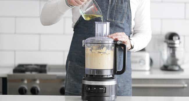 adding olive oil to a food processor of hummus