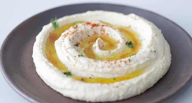 sprinkling parsley and cayenne pepper onto a plate of hummus