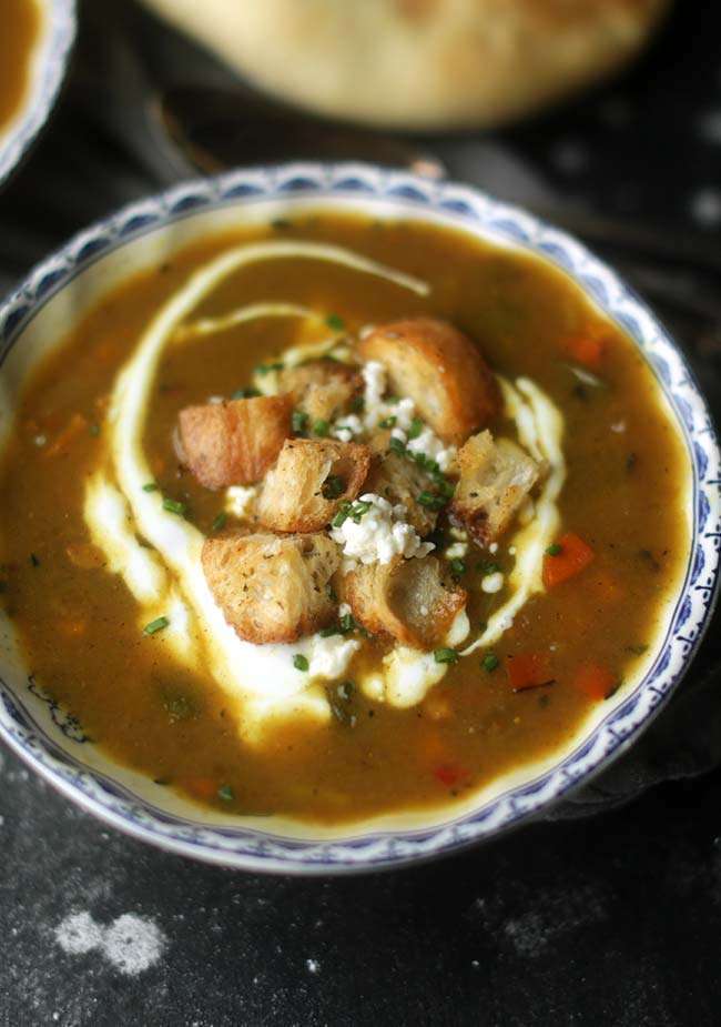 Indian mulligatawny soup garnished with croutons, goat cheese and chives