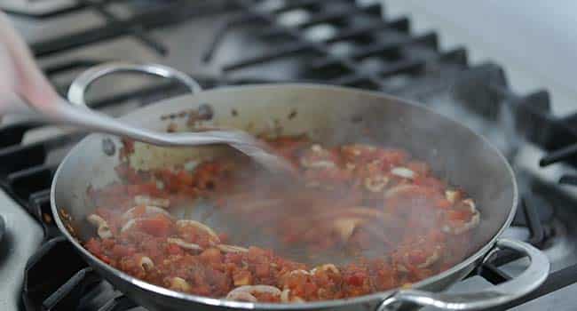 cooking tomatoes and squid with sofrito in a pan