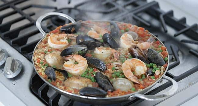adding seafood to a pan with rice to make paella