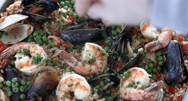 garnishing a pan of seafood and chicken paella with cilantro