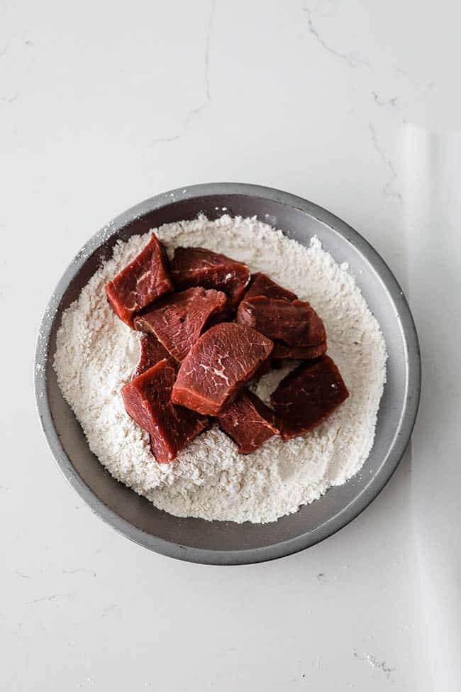 cubed beef in a pan with seasoned flour