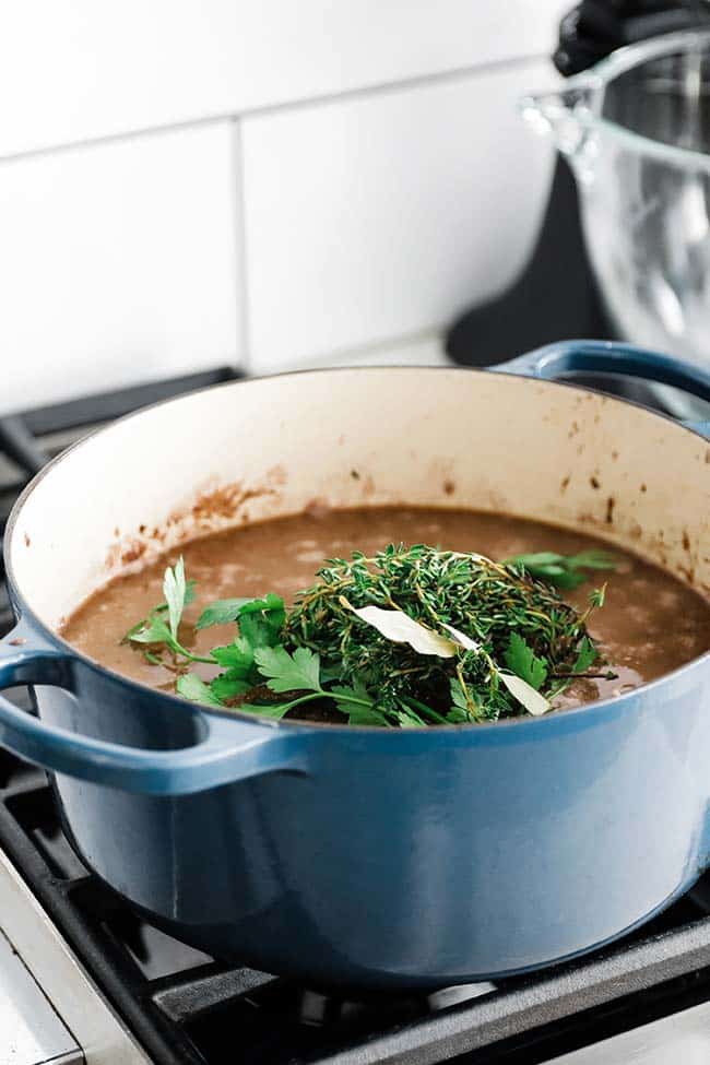 a large pot with beef stock and fresh herbs