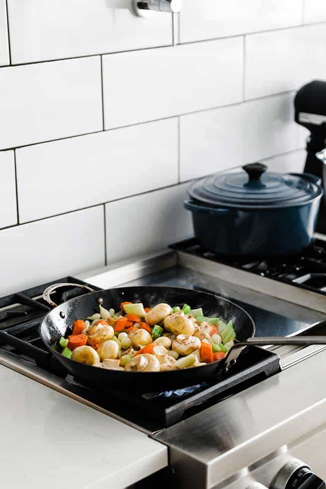 cut vegetables and mushrooms cooking in a large frying pan