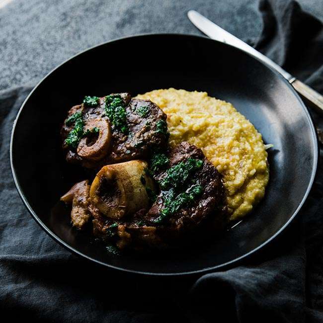 veal osso bucco shanks in a bowl next to polenta and topped off with gremolata