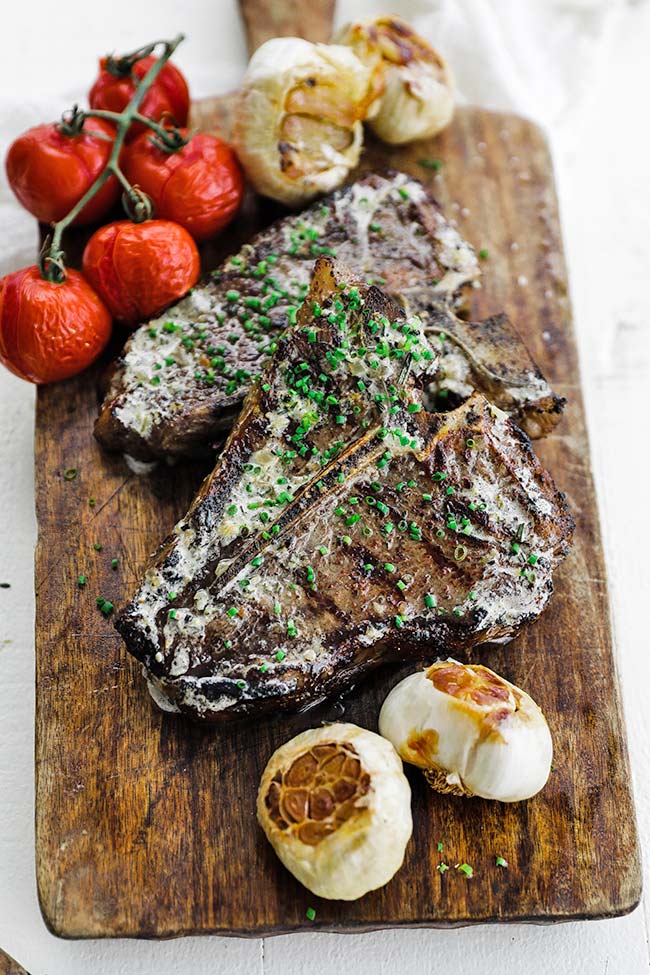grilled t bone steaks with butter and roasted garlic on a cutting board