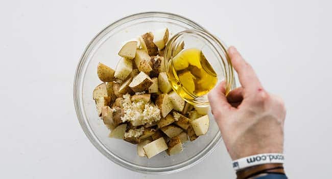 Adding garlic and olive oil to potatoes in a bowl