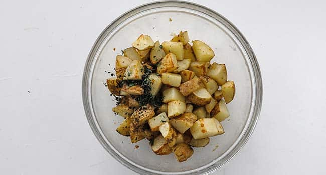 tossing potatoes in a bowl with fresh oregano