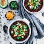 bowls of chili topped off with sour cream and avocados next to other toppings