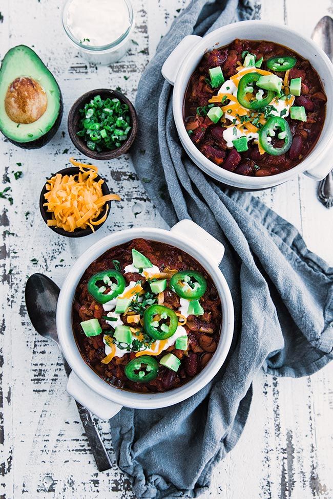 bowls of chili topped off with sour cream and avocados next to other toppings