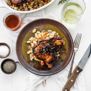 roasted pork chop on a plate with beans and vegetables