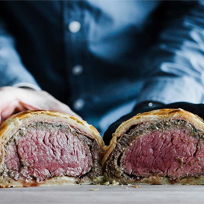 beef wellington sliced in half on a cutting board
