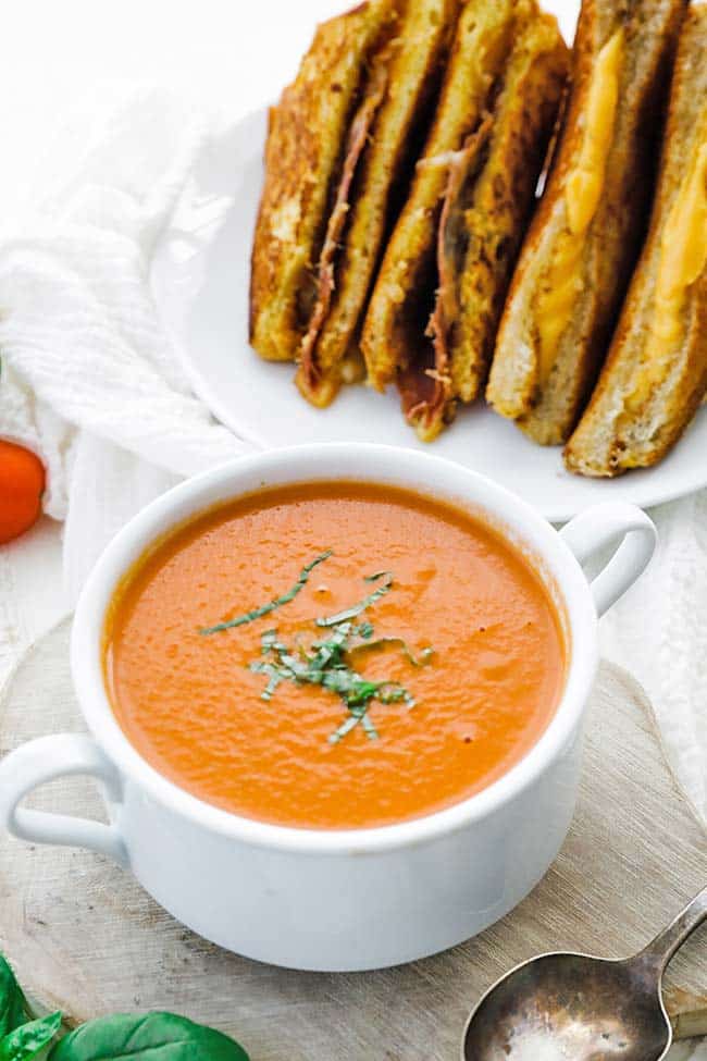 tomato soup in a bowl with fresh basil on a cutting board