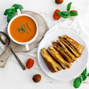 sliced grilled cheese on a plate next to a bowl of tomato soup