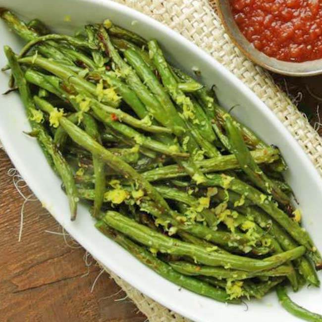 oval dish full of cooked green beans with lemon zest