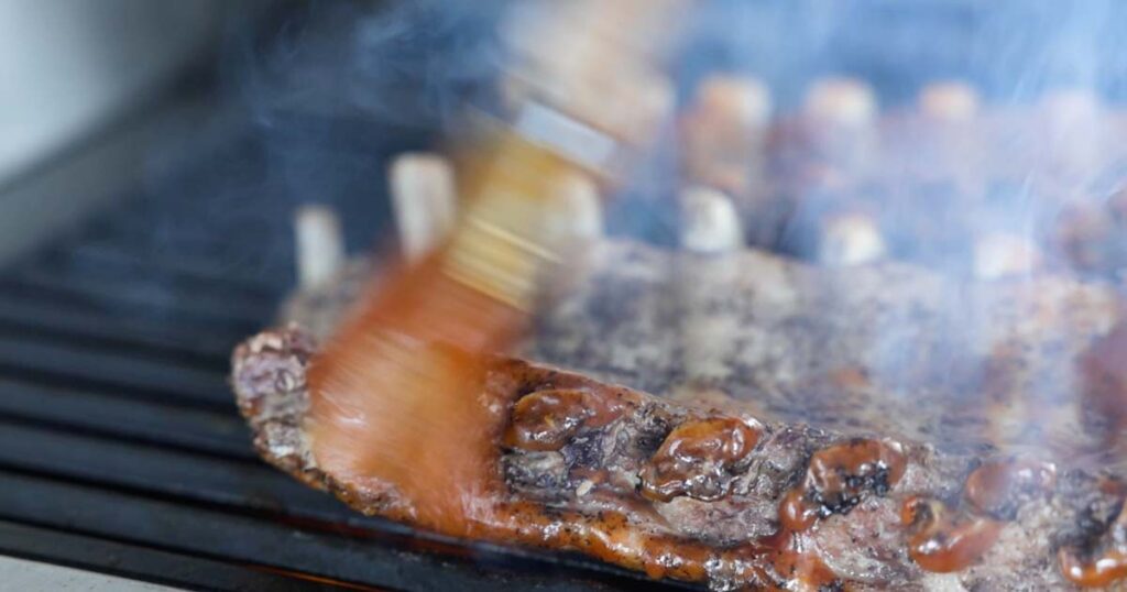 brushing ribs with bbq sauce on a grill