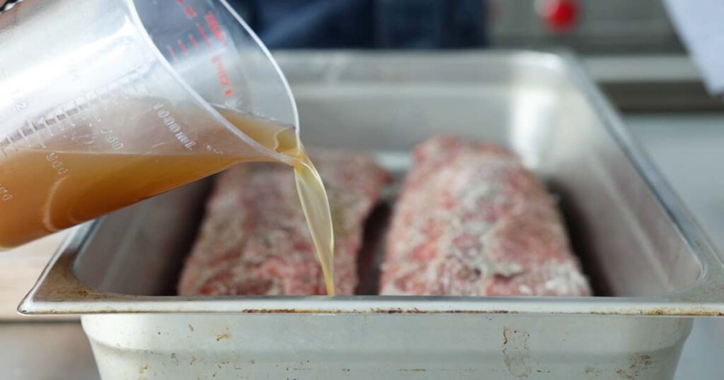 pouring beef stock into a pan with ribs