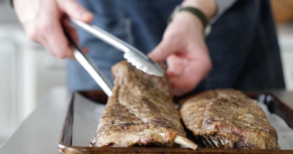 adding baked ribs to a sheet tray lined with parchment paper