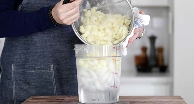 adding boiled potatoes to a container full of ice water