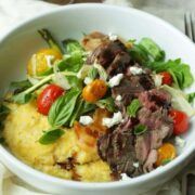 sliced steak with bacon, herbs, roasted tomatoes and polenta in a white bowl