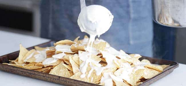 pouring a cheese sauce all over corn chips