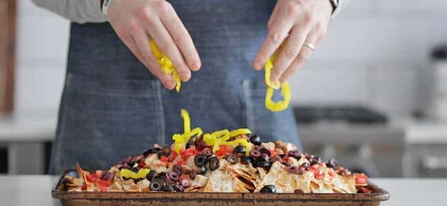 adding peppers to chips with olives and tomatoes