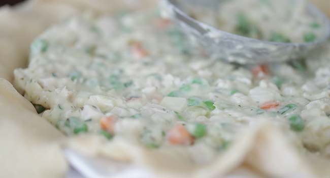 adding turkey pot pie filling into a pie