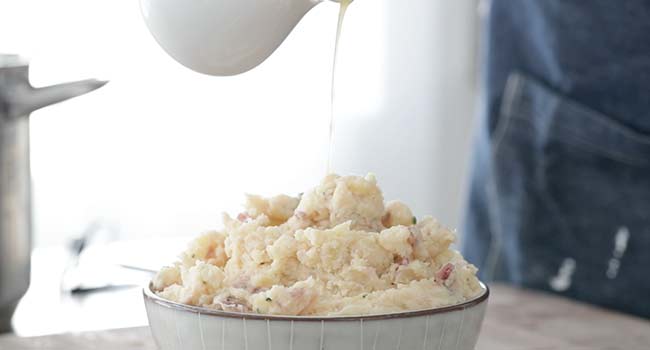 pouring melted butter on horseradish mashed potatoes