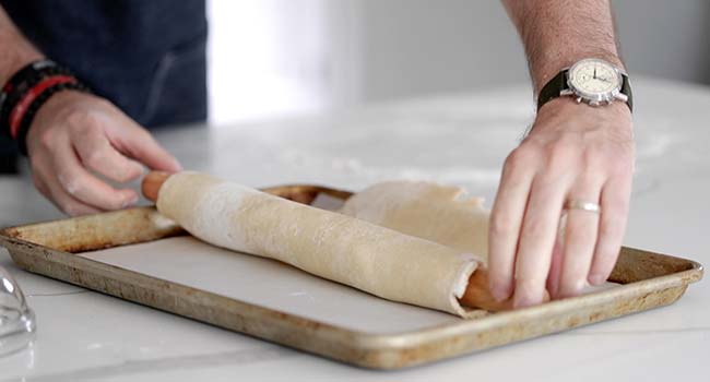 placing rolled out dough onto a cookie sheet tray with parchment paper