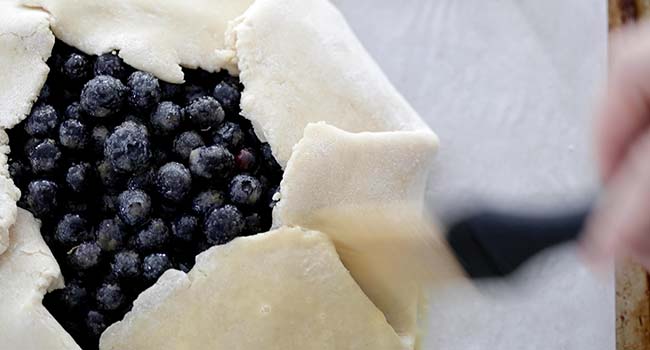 brushing a blueberry crostata with egg wash