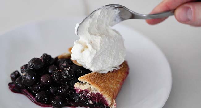 serving whipped cream with a blueberry crostata slice