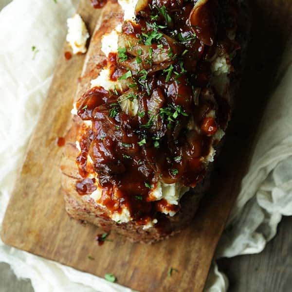 bbq sauce and onions covering mashed potatoes and meatloaf on a cutting board