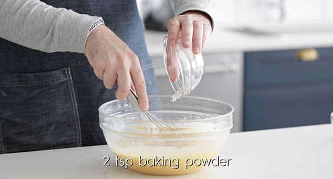 pouring cinnamon and baking powder into a bowl with mashed bananas