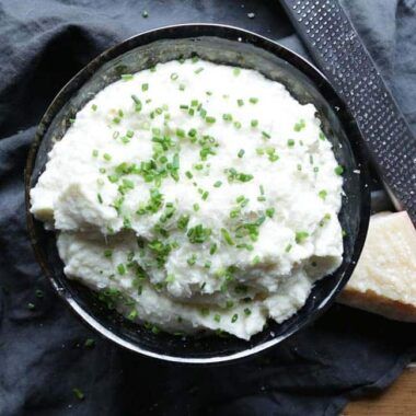 mashed cauliflower in a bowl with chives and parmesan cheese