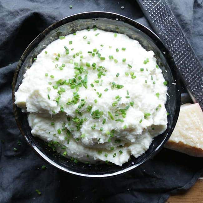 mashed cauliflower in a bowl with chives and parmesan cheese