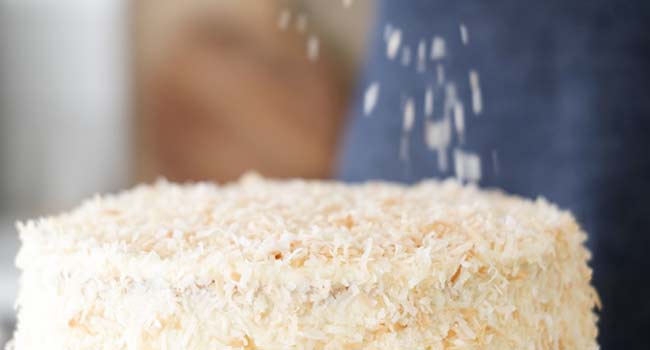 adding toasted coconut to a coconut cake