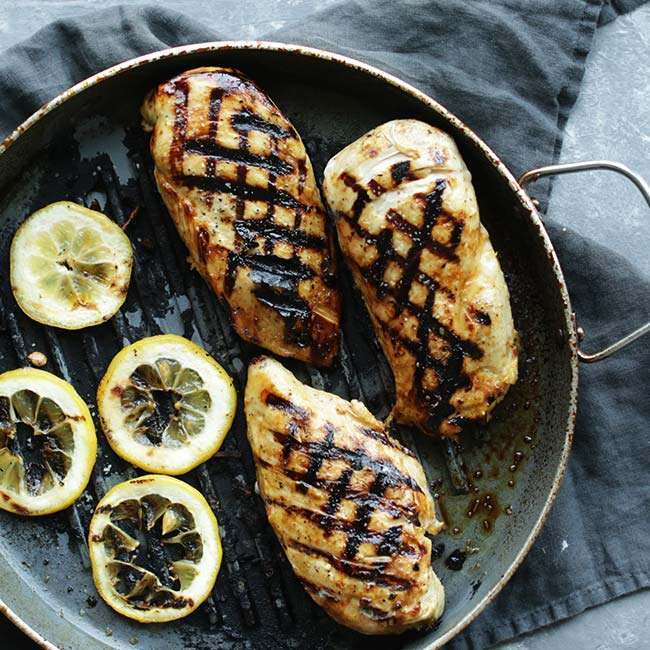 grilled chicken breasts in a grill pan with lemon wheels