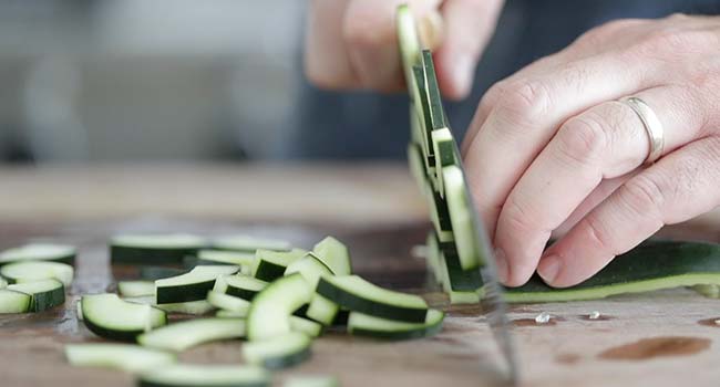 thinly slicing fresh cucumbers on a cutting board