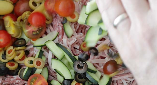 Adding prepared vegetables to a large bowl of cooked pasta