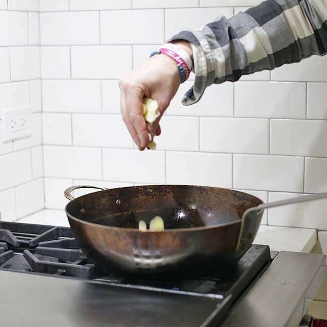 adding garlic and anchovies to a large pan