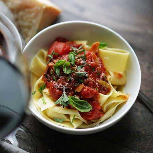 bowl of homemade pappardelle pasta topped off with a tomato sauce and herbs