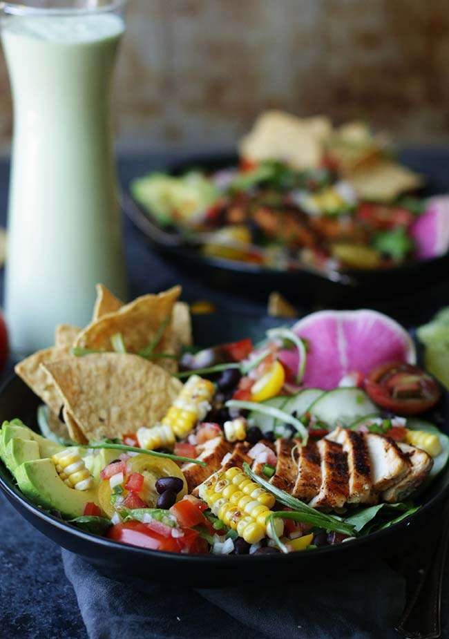 bowl of taco salad with tortillas, corn and chicken with a jar of avocado lime dressing