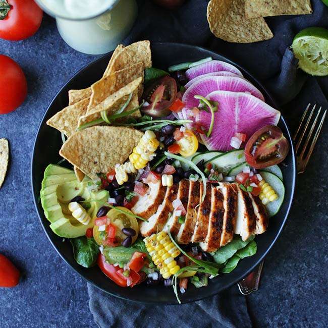 bowl of vegetables with chicken, tortilla chips, avocado, corn, tomatoes and greens