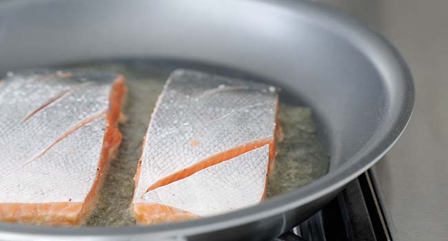 adding salmon to a pan with hot oil