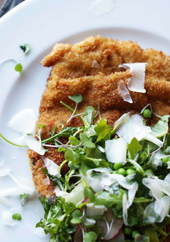 breaded and fried pork chop on a plate with salad and parmesan cheese